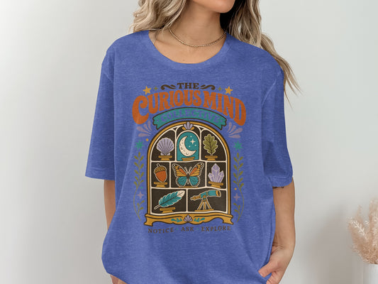 Blue t-shirt with "The Curious Mind Collective" and art of objects in a window.