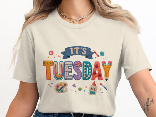 Cream t-shirt with "IT'S TUESDAY" embroidered with craft supplies.