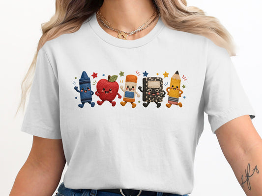 White t-shirt with embroidered cartoon crayon, apple, eraser, notebook, and pencil.