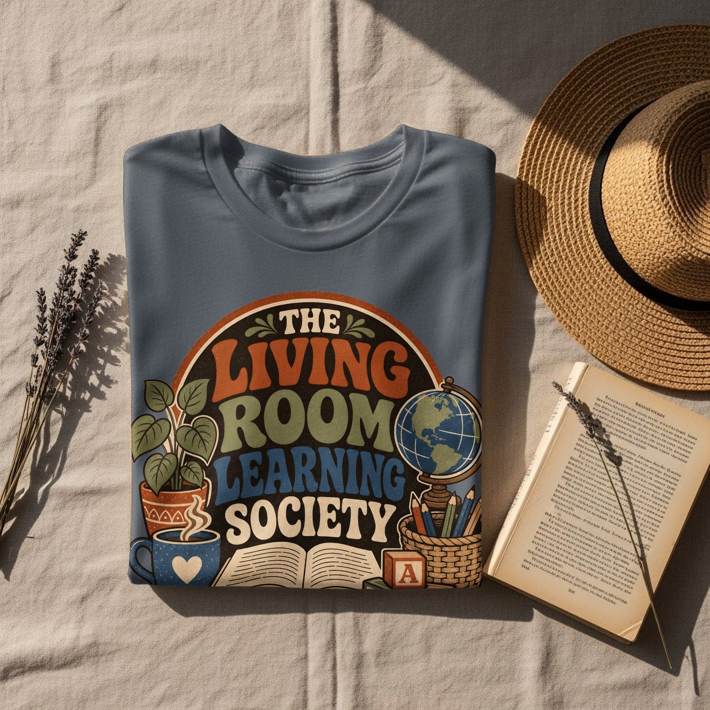 Blue t-shirt with "The Living Room Learning Society" text, illustrations of plants, books, and a globe.