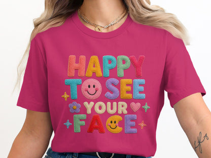 Pink t-shirt with "HAPPY TO SEE YOUR FACE" in colorful felt letters and icons.