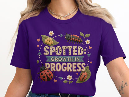 Purple t-shirt with spotted design, ladybug, caterpillar, and text "SPOTTED: GROWTH IN PROGRESS".