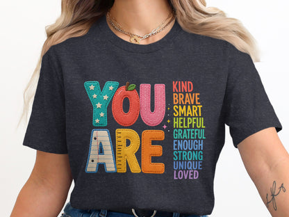 "YOU ARE" text with positive affirmations in rainbow colors on a charcoal t-shirt.