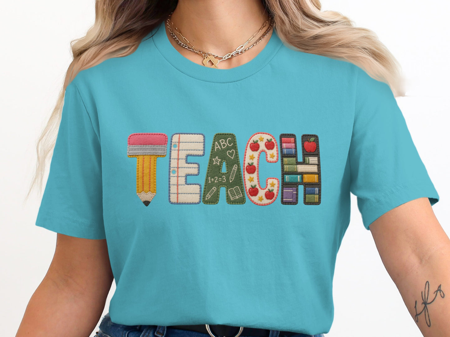 Teal t-shirt with "TEACH" embroidered with school-themed letters and icons.