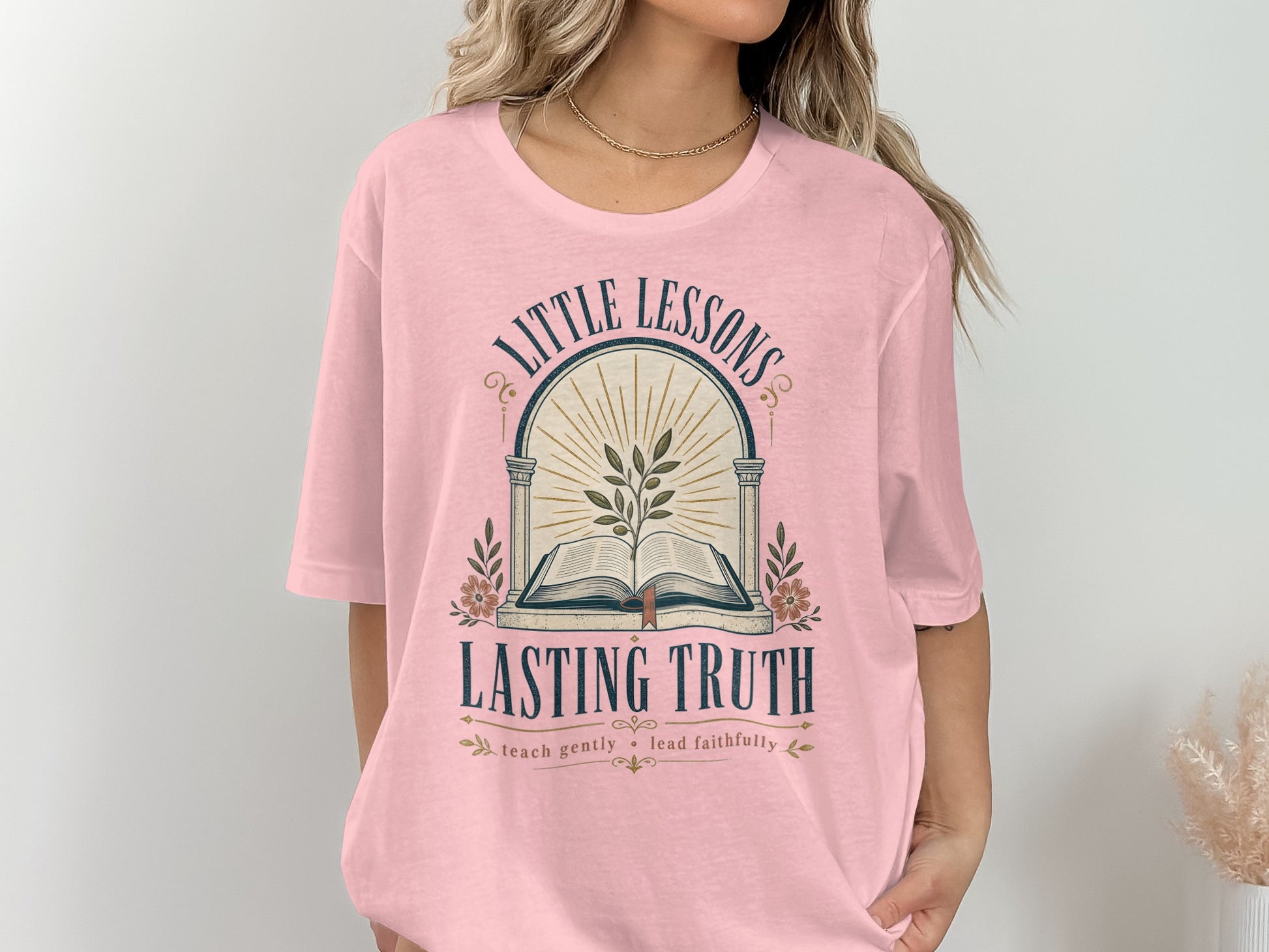 Pink t-shirt with "Little Lessons Lasting Truth" graphic featuring an open book and plant.