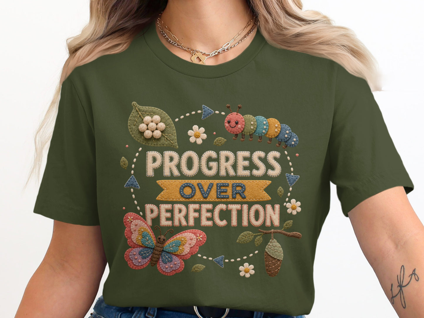 Green t-shirt graphic with embroidered caterpillar and butterfly, text "Progress Over Perfection".