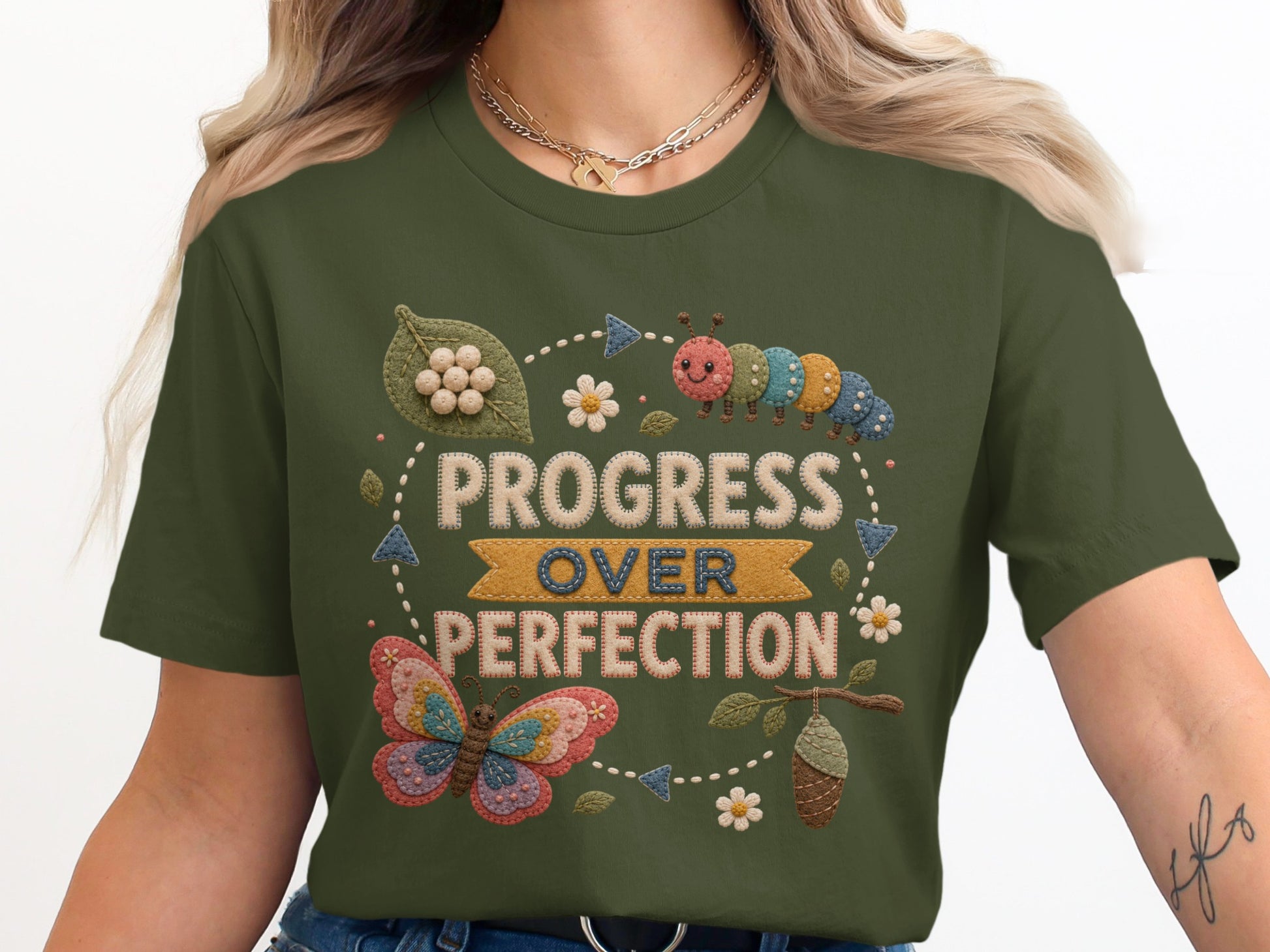 Green t-shirt graphic with embroidered caterpillar and butterfly, text "Progress Over Perfection".