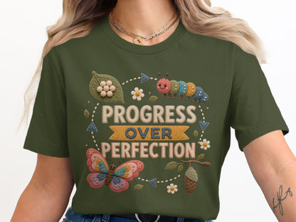 Green t-shirt graphic with embroidered caterpillar and butterfly, text "Progress Over Perfection".