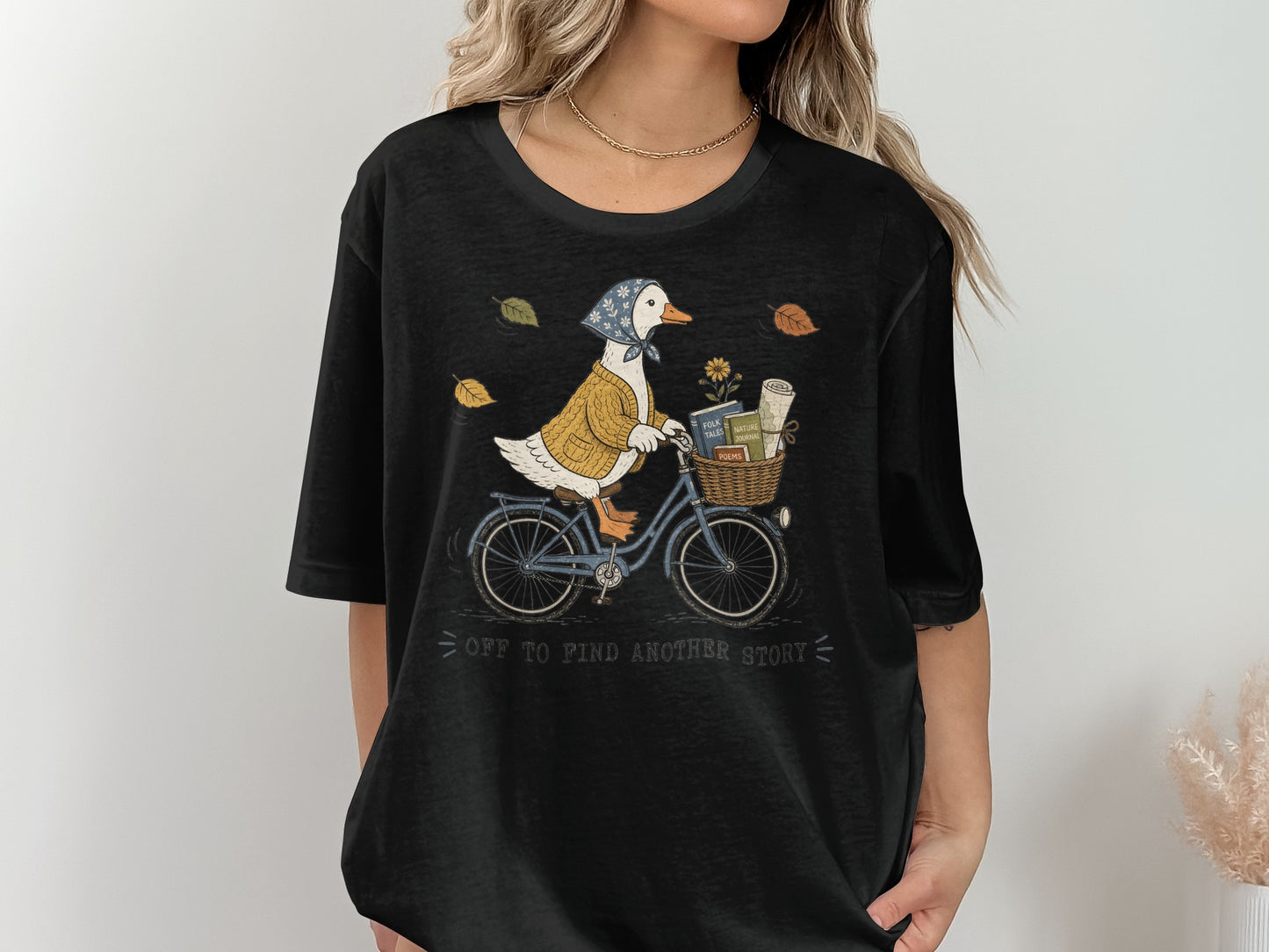 Duck in sweater and bandana rides blue bike with basket of books, text reads "off to find another story".