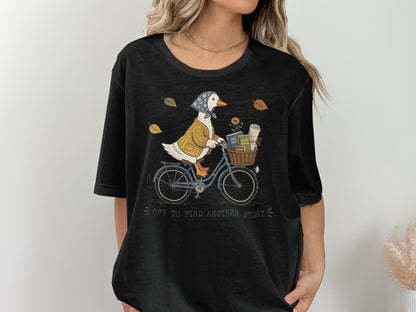 Duck in sweater and bandana rides blue bike with basket of books, text reads "off to find another story".