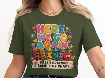 Green t-shirt with "HERE WE GO AGAIN" text and cartoon crayons, apple, and coffee.
