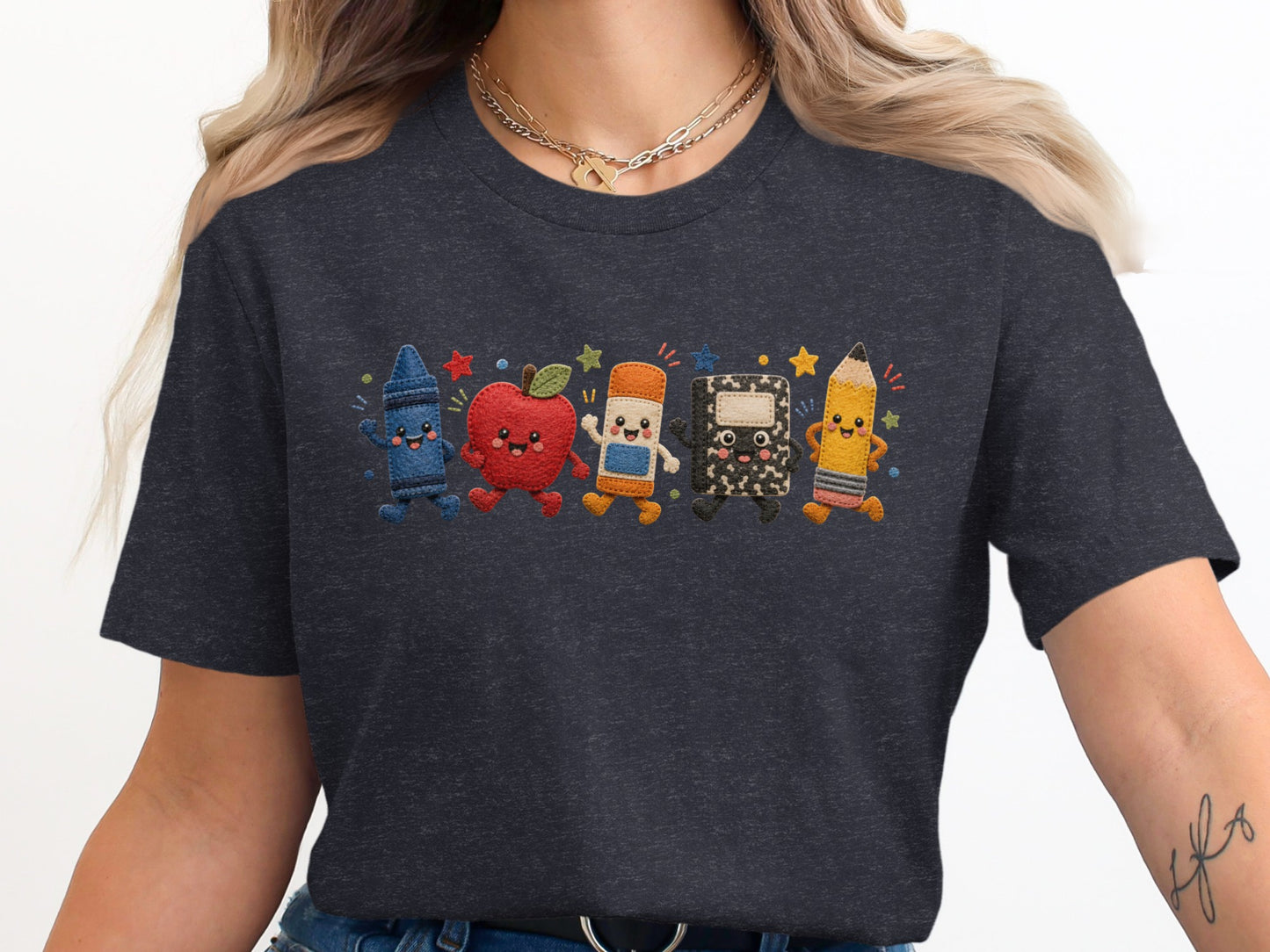 Cute embroidered cartoon crayon, apple, eraser, notebook, and pencil walking on dark grey t-shirt.