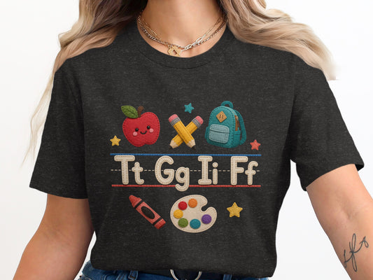 T-shirt with apple, pencils, backpack, crayon, and paint palette graphic.