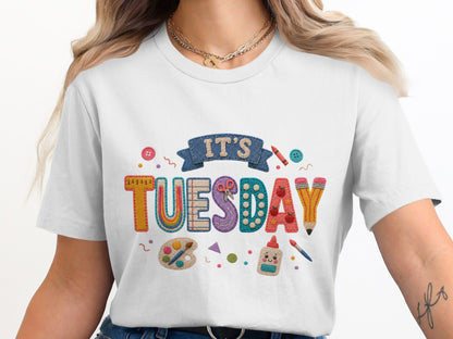 White t-shirt with colorful "IT'S TUESDAY" text and school supplies graphics.