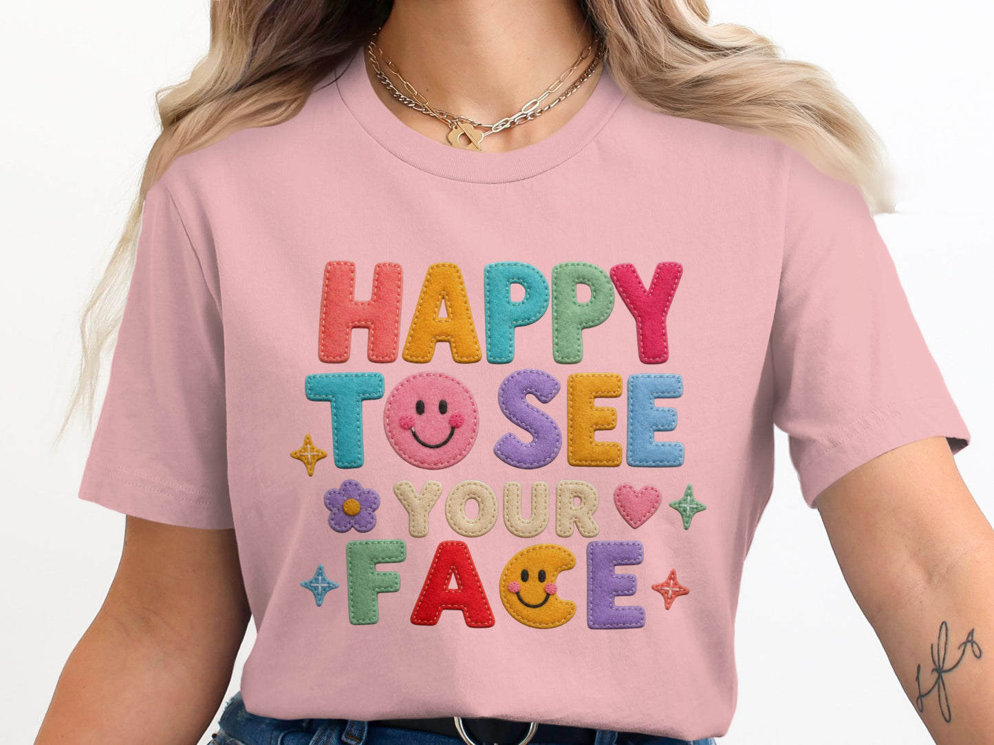 Pink t-shirt with colorful "HAPPY TO SEE YOUR FACE" text and playful icons.