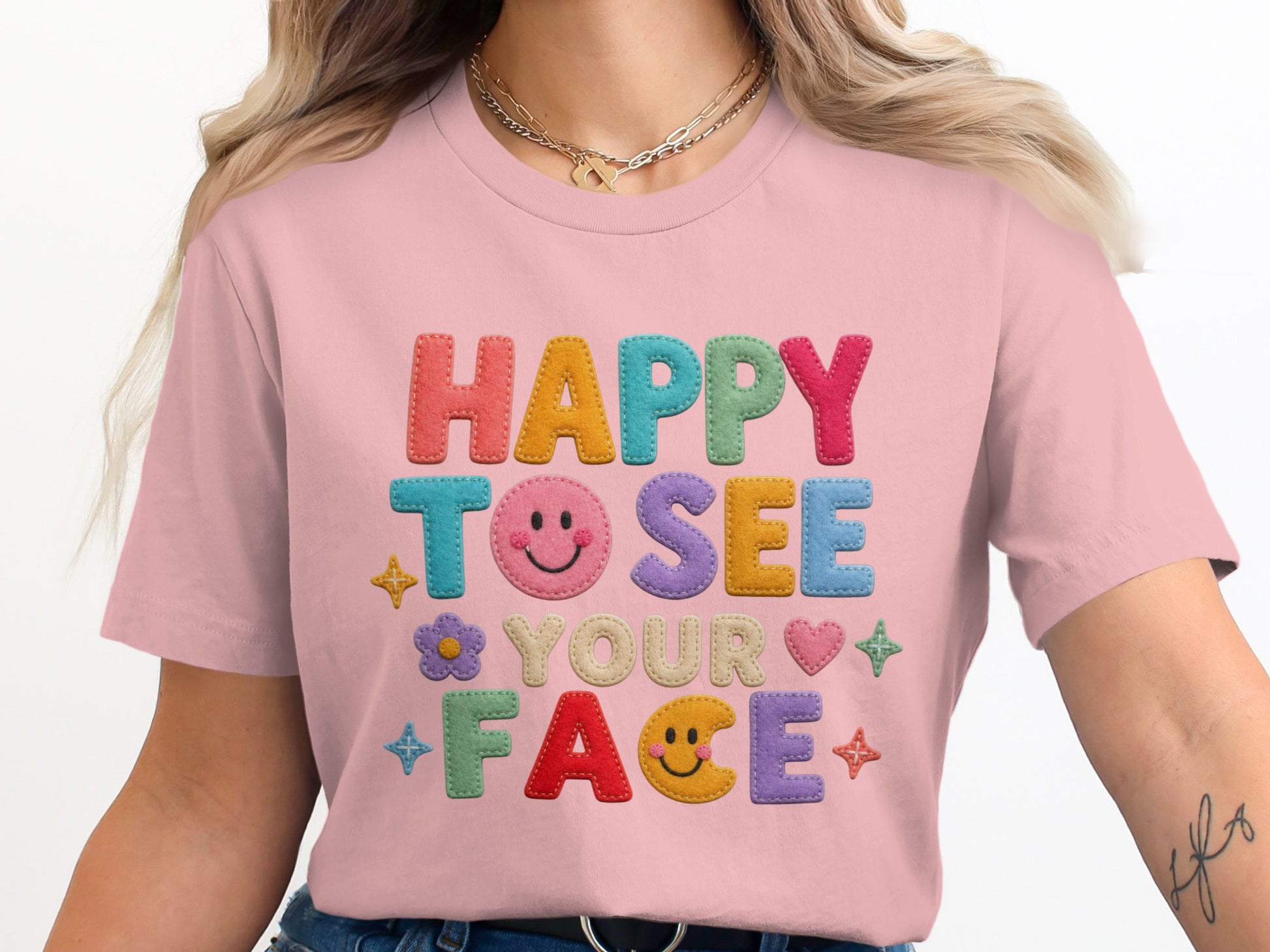 Pink t-shirt with colorful "HAPPY TO SEE YOUR FACE" text and playful icons.