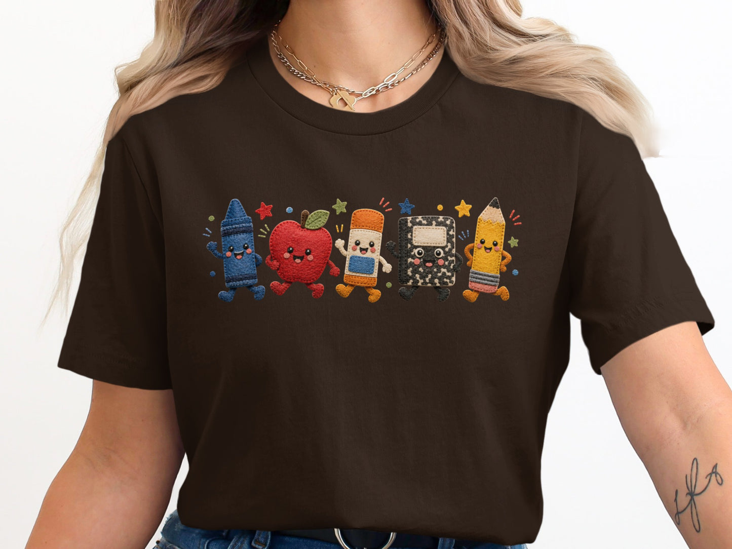 Brown t-shirt with embroidered cartoon school supplies including a crayon, apple, and pencil.