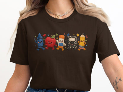 Brown t-shirt with embroidered cartoon school supplies including a crayon, apple, and pencil.