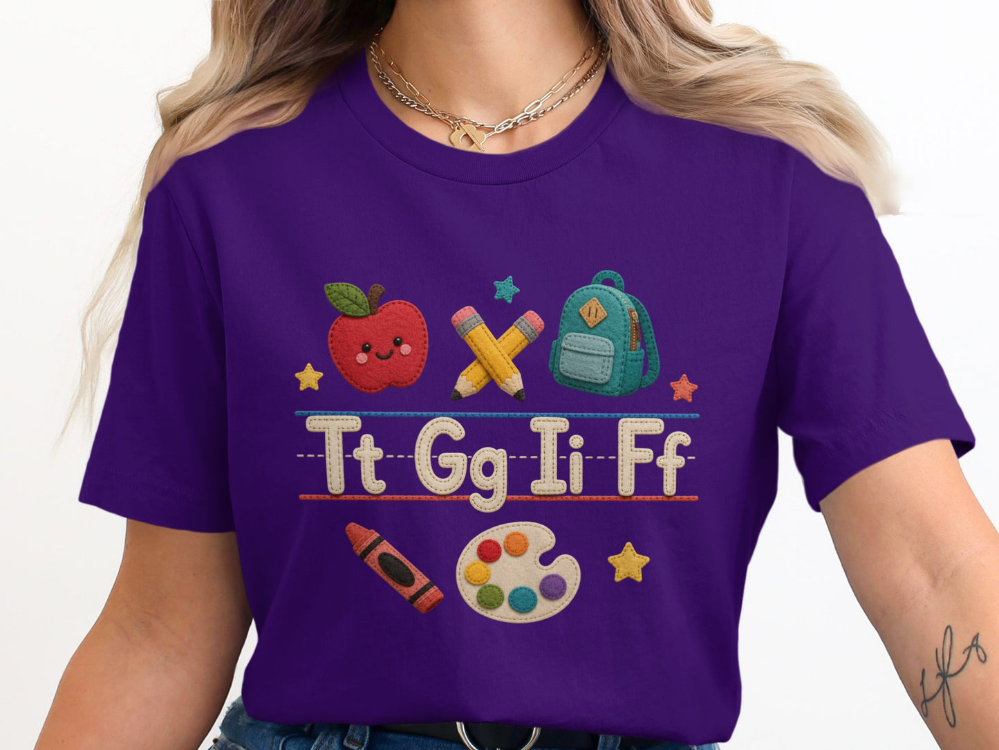 Purple t-shirt with embroidered alphabet letters, apple, backpack, pencils, crayon, and paint palette.