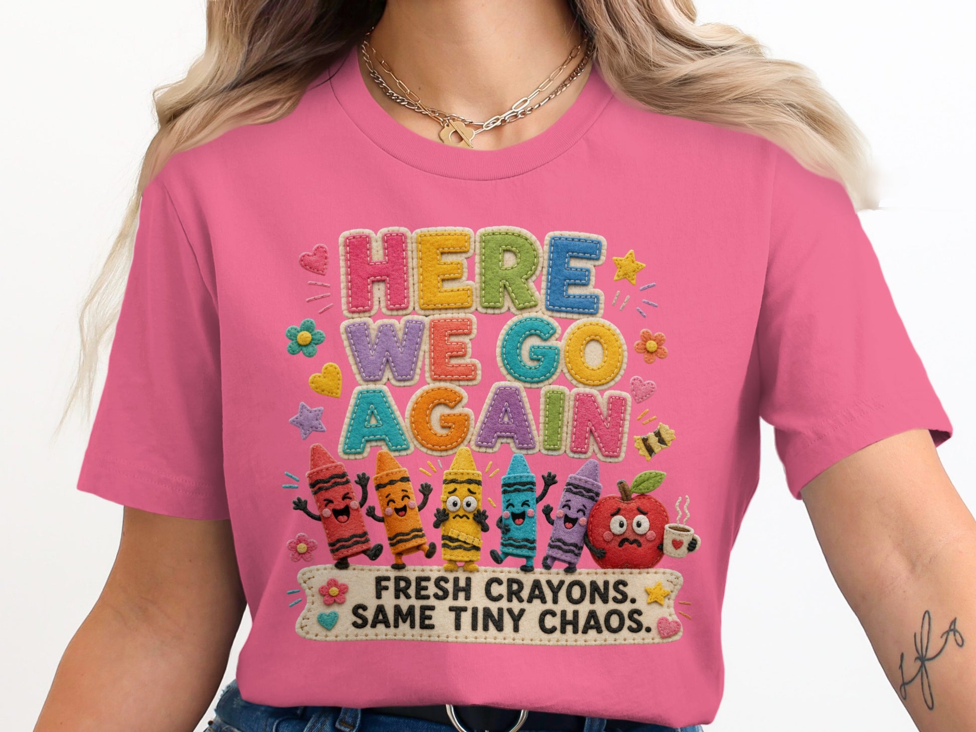 Pink shirt with "HERE WE GO AGAIN" text above cartoon crayons and an apple.
