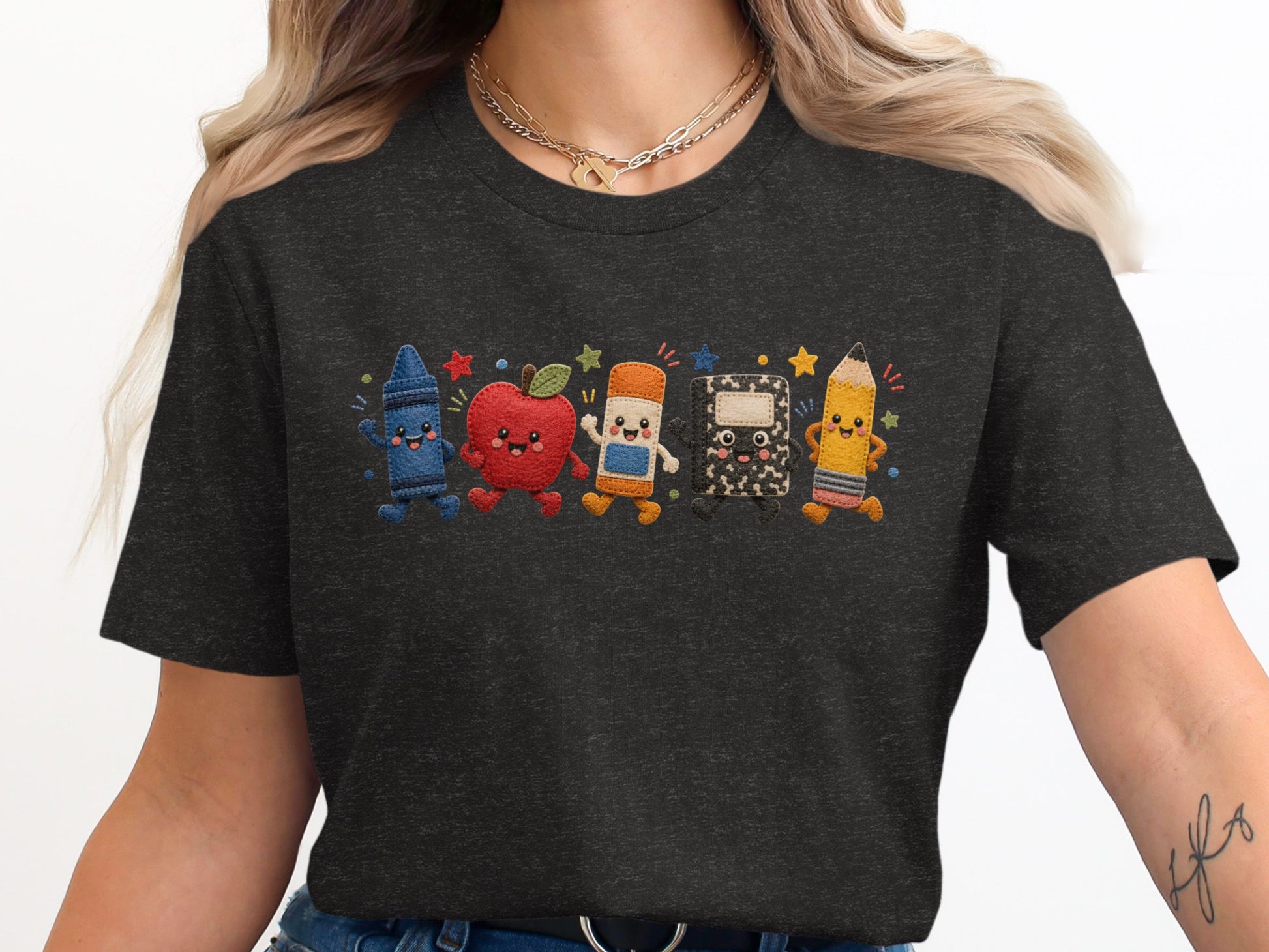 Dark t-shirt with embroidered crayon, apple, eraser, notebook, and pencil characters.