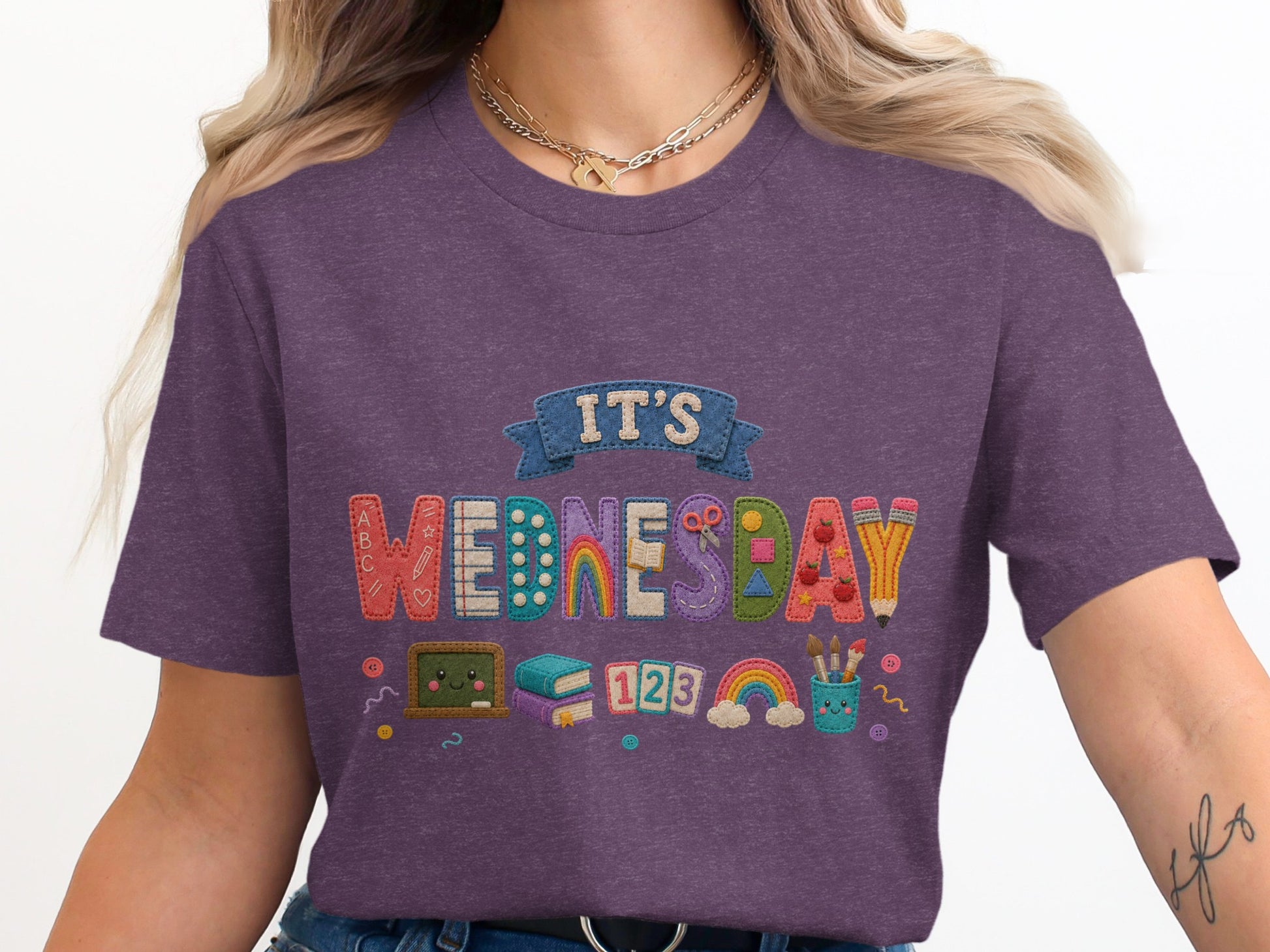 It's Wednesday text with school supplies, books, and rainbows on a purple shirt.