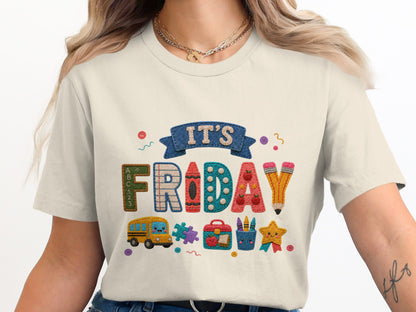 It's Friday graphic with school supplies, bus, and star on a cream t-shirt.