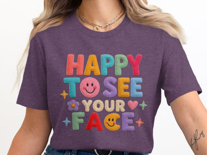 Purple t-shirt with "HAPPY TO SEE YOUR FACE" text in colorful embroidered letters.