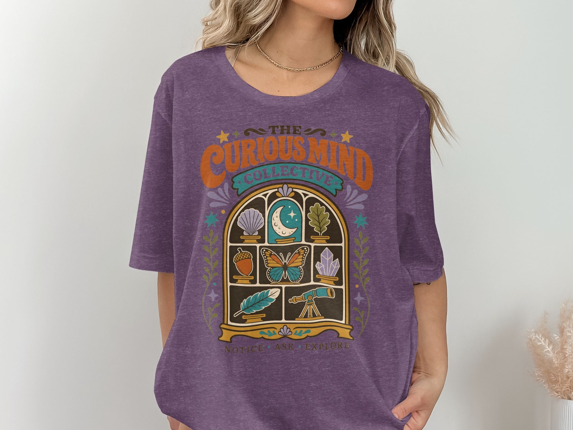 Purple t-shirt with "The Curious Mind Collective" and window illustration.