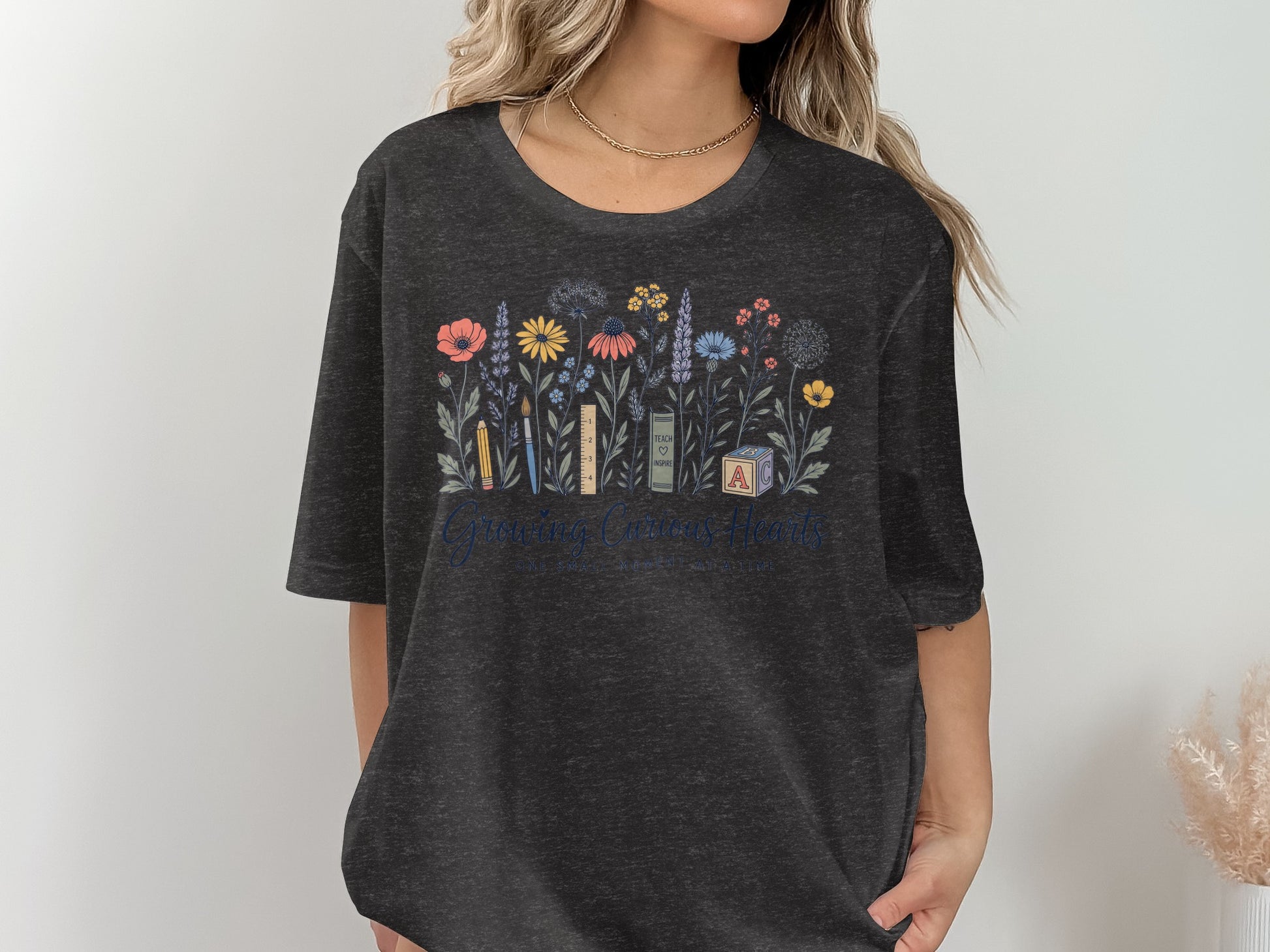 Dark grey t-shirt with floral and school supply art, "Growing Curious Hearts" text.