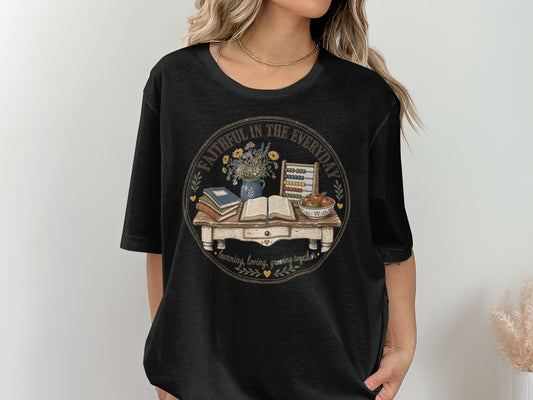 Black t-shirt with a circular graphic featuring a desk with books, flowers, abacus, and fruit.