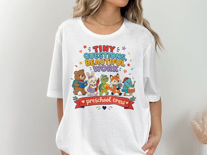 White t-shirt with colorful cartoon animals and "tiny questions, beautiful work, preschool crew" text.