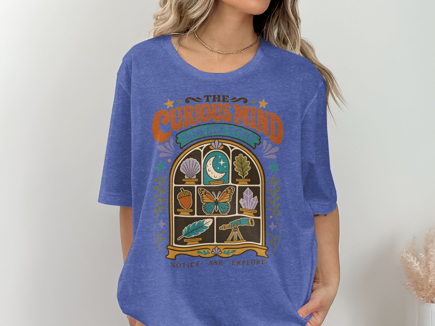 Blue t-shirt with "The Curious Mind Collective" and art of objects in a window.
