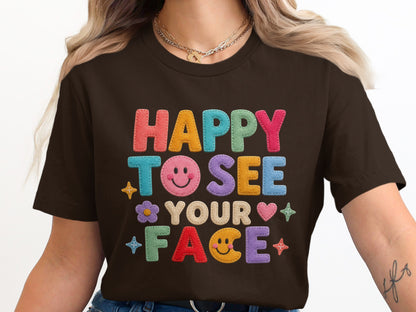 Brown t-shirt with "HAPPY TO SEE YOUR FACE" in colorful applique letters and icons.