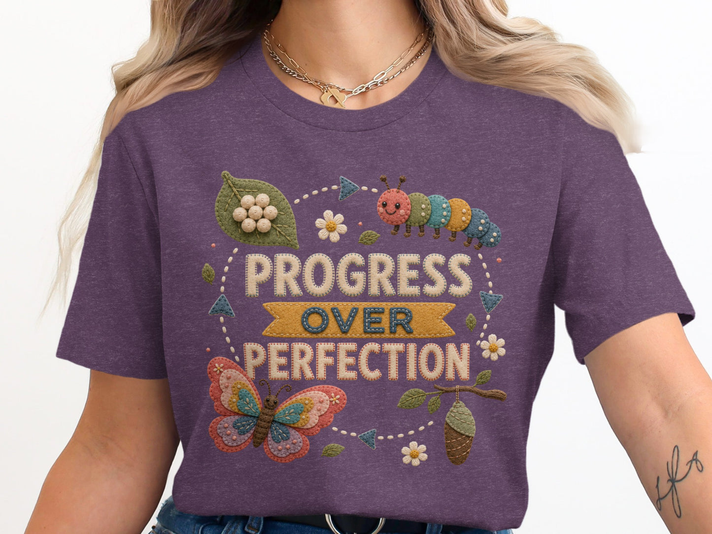 Purple t-shirt with embroidered butterfly, caterpillar, and "PROGRESS OVER PERFECTION" text.