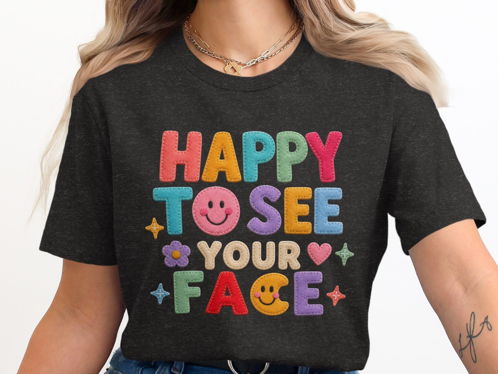Dark t-shirt with colorful felt lettering reading "HAPPY TO SEE YOUR FACE" with smiley faces.
