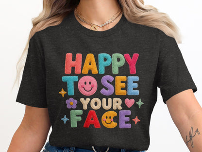 Dark t-shirt with colorful felt lettering reading "HAPPY TO SEE YOUR FACE" with smiley faces.