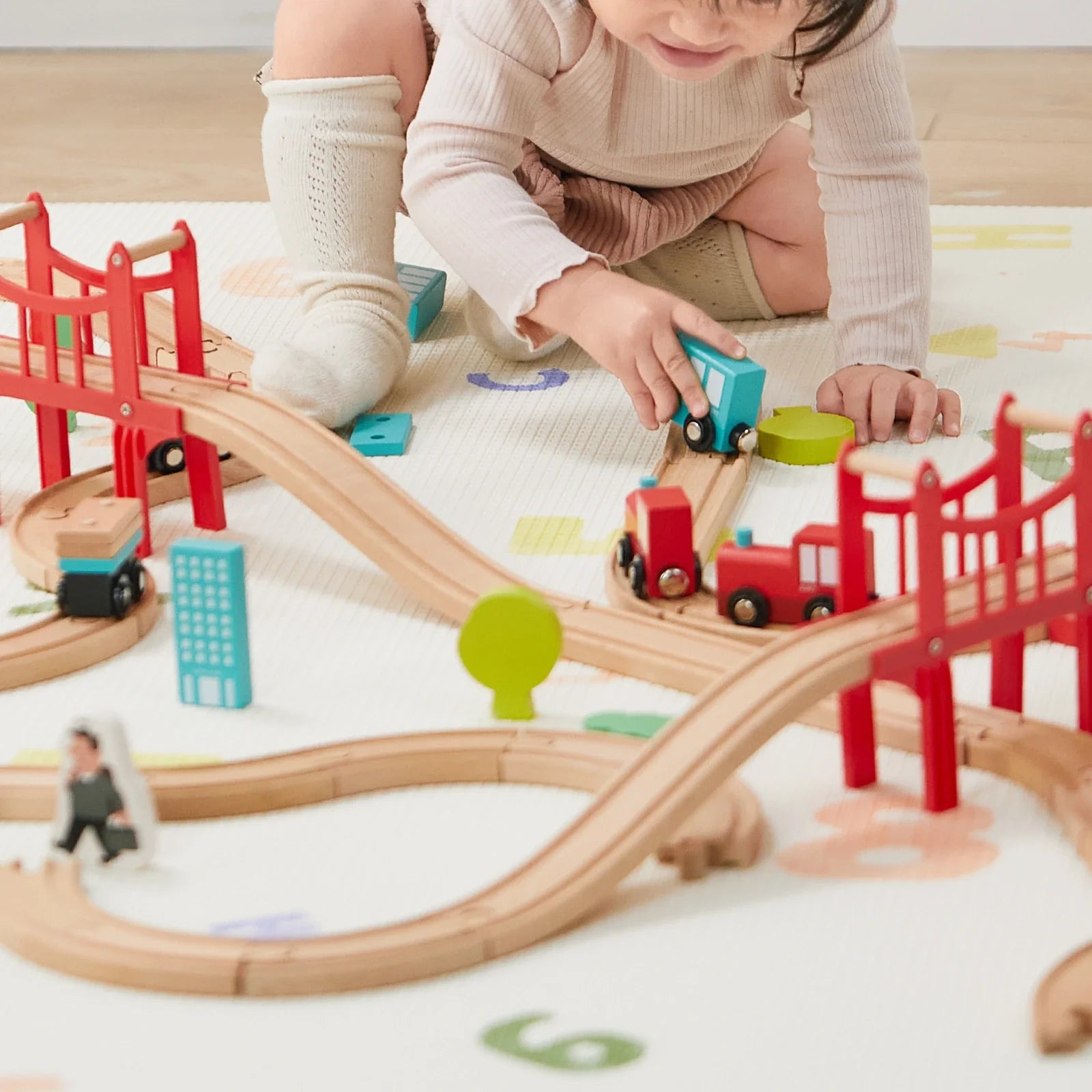 Preschooler playing with wooden train set on floor, building track layout