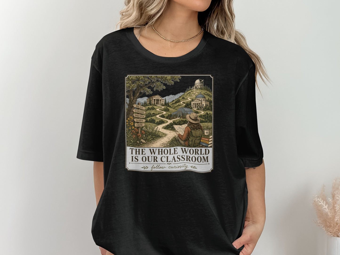 T-shirt graphic with pathway through nature to buildings, mountains, and observatory. Text: "THE WHOLE WORLD IS OUR CLASSROOM follow curiosity".