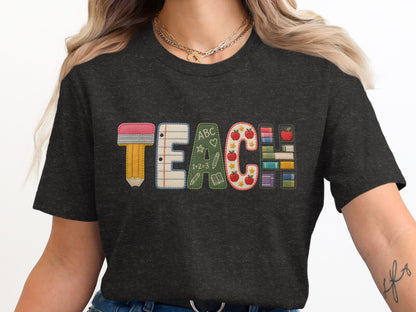 Embroidered TEACH graphic on dark grey t-shirt with pencil, notebook, apple, and book elements.