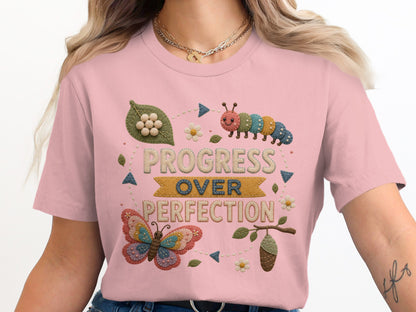 Pink t-shirt with embroidered "Progress Over Perfection" text, caterpillar, butterfly, and chrysalis.