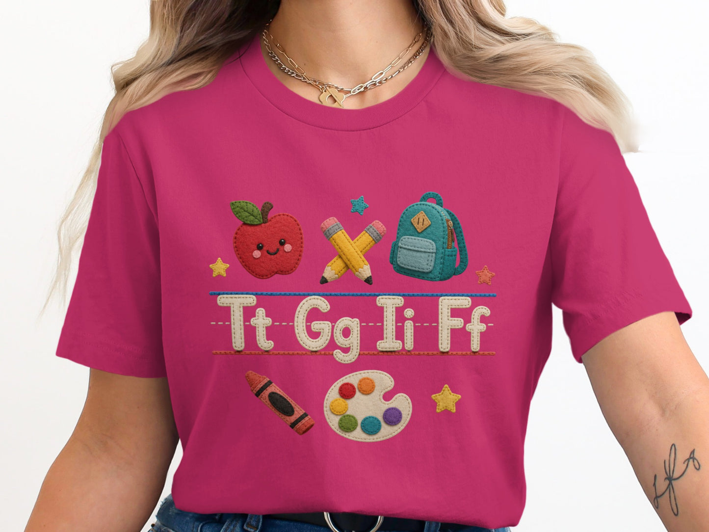 Pink t-shirt with embroidered apple, backpack, pencils, Tt Gg Ii Ff text, crayon, and paint palette.