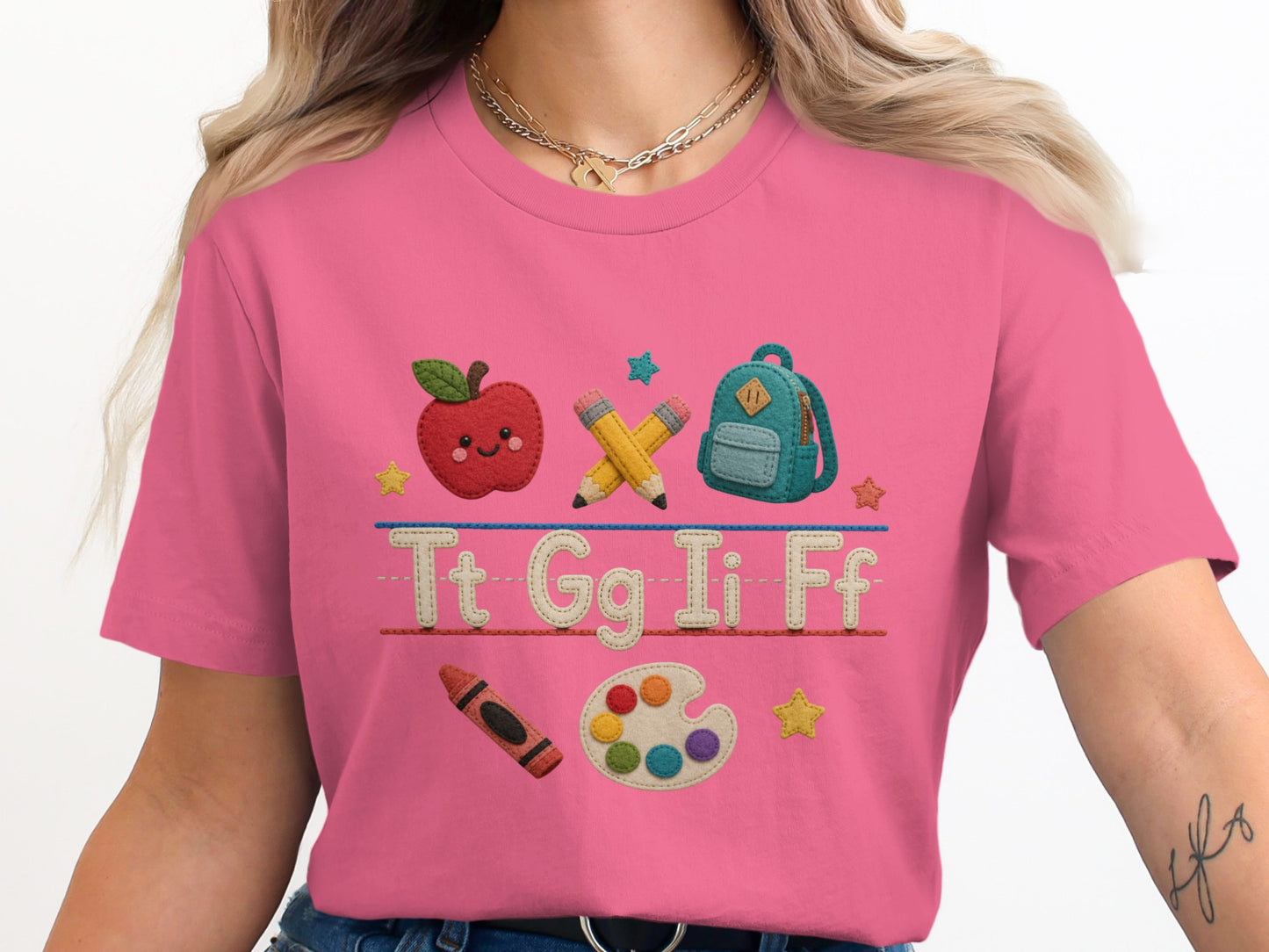 Pink t-shirt with embroidered school icons: apple, pencils, backpack, crayon, paint palette, and letters Tt Gg Ii Ff.