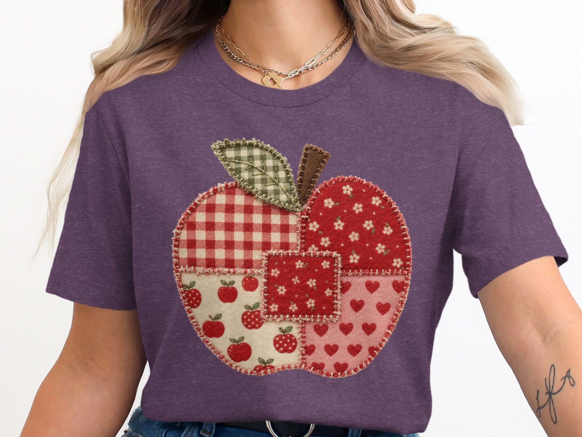 Purple t-shirt with a patchwork apple graphic featuring gingham, floral, apple, and heart patterns.