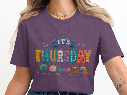 Purple t-shirt with "It's Thursday" design and school-themed applique graphics.