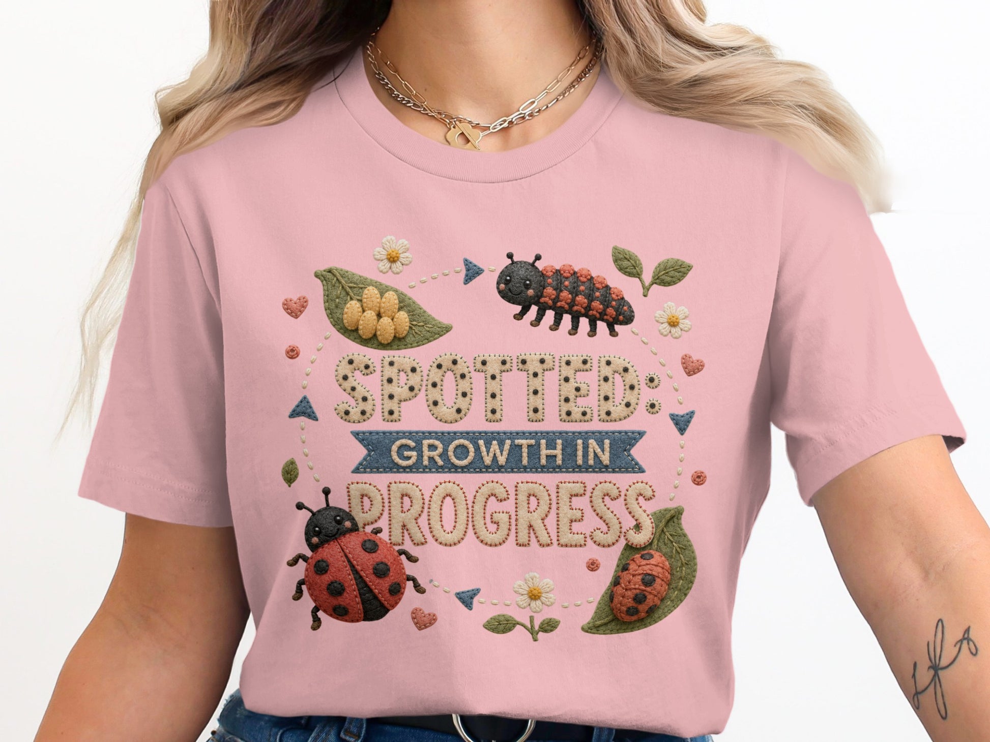 Pink t-shirt featuring embroidered "Spotted: Growth in Progress" with ladybugs and caterpillar.