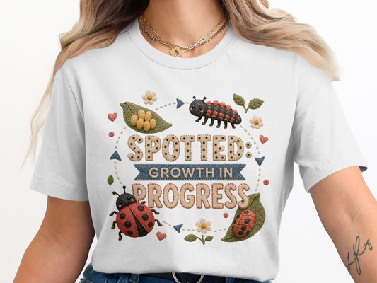White t-shirt graphic with a caterpillar, ladybugs, and the text "SPOTTED: GROWTH IN PROGRESS".