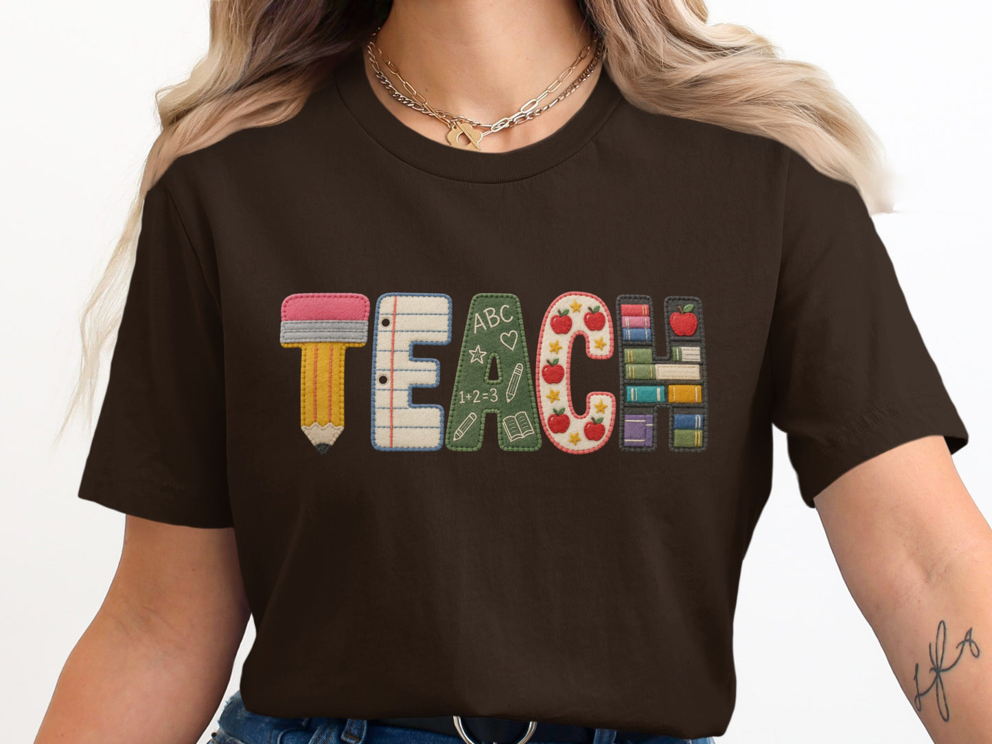 Brown t-shirt with embroidered letters spelling TEACH with school-themed graphics.