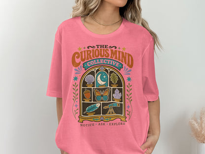 Pink t-shirt features "The Curious Mind Collective" logo with moon, butterfly, feather, and telescope.