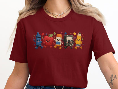 Maroon t-shirt with embroidered cartoon crayon, apple, pencil, eraser, and notebook.